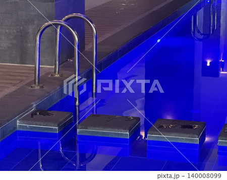 Blue ambient lighting illuminating indoor swimming pool ladder and tiled lanes at night background Blue ambient lighting illuminating indoor swimming pool ladder and tiled lanes at night background 140008099