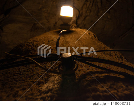 Close up of an artificial light bulb illuminating a dark underground cave corridor. Close up of an artificial light bulb illuminating a dark underground cave corridor. 140008731