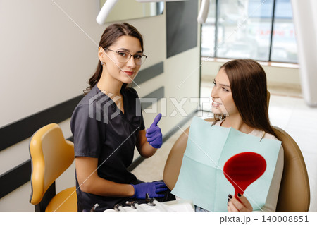 Woman is happy with results after oral hygiene and teeth whitening at dentist office. Patient is smiling and looking at the mirror 140008851