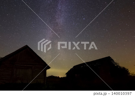 Starry sky over wooden houses in the village. Starry sky background picture of stars in night sky and the Milky Way. Starry sky over wooden houses in the village. Starry sky background picture of stars in night sky and the Milky Way. 140010397
