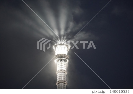幻想的な光の冠：夜の東京スカイツリー最上部と雲を照らすサーチライト 140010525