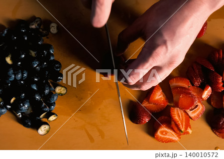 Blueberries and strawberries on the table, cutting strawberries with knife. 140010572