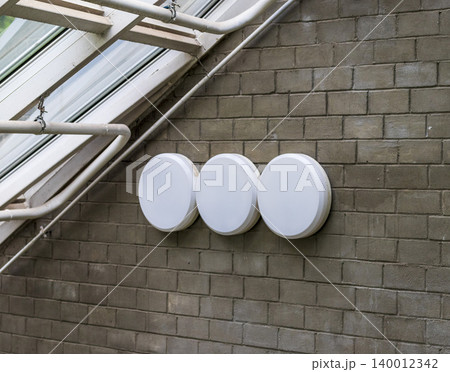A series of modern, round bulkhead light fixtures mounted on an industrial brick wall. A series of modern, round bulkhead light fixtures mounted on an industrial brick wall. 140012342