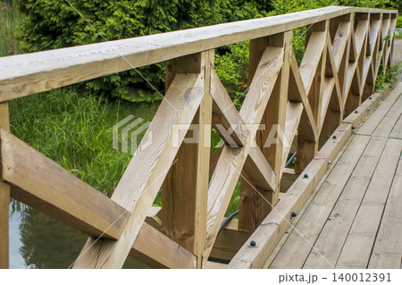 Wooden pedestrian footbridge over a calm pond in a green park. Outdoor Wooden pedestrian footbridge over a calm pond in a green park. Outdoor 140012391