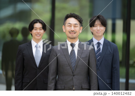 ビル背景で管理職や社長、リーダーの髭の上司と若手社員が並ぶ組織力と人材育成のビジネスチームイメージ 140012482