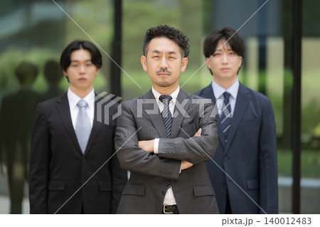 ビル背景で管理職や社長、リーダーの髭の上司と若手社員が並ぶ組織力と人材育成のビジネスチームイメージ 140012483