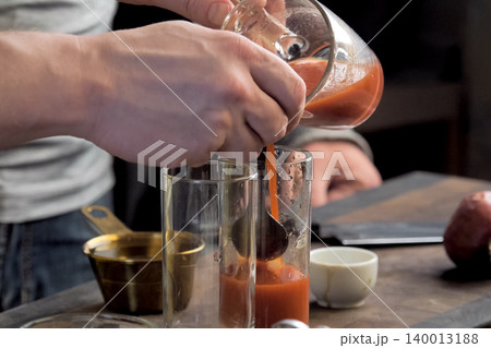 Pouring tomato juice into glasses through spoon. 140013188