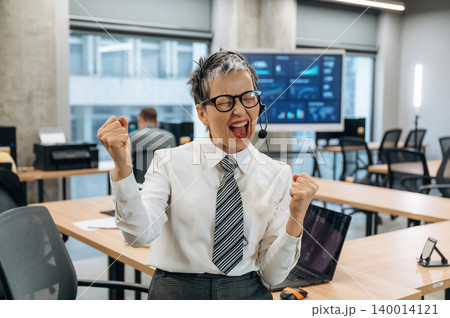 Businesswoman celebrating success in modern office environment, wearing headset and formal attire, showcasing enthusiasm and professional achievement in corporate setting Businesswoman celebrating success in modern office environment, wearing headset and formal attire, showcasing enthusiasm and professional achievement in corporate setting 140014121