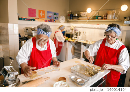 Senior African American and Caucasian women chefs preparing pastries in a professional kitchen bakery 140014194