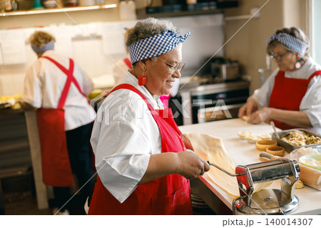 Happy Senior Black Woman Preparing Fresh Pasta Dough in a Commercial Kitchen with Coworkers Happy Senior Black Woman Preparing Fresh Pasta Dough in a Commercial Kitchen with Coworkers 140014307