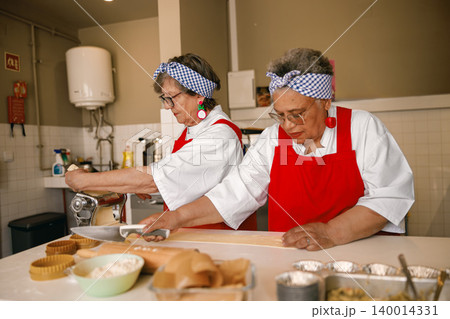 Diverse Caucasian and multiracial seniors preparing fresh dough in a professional kitchen 140014331