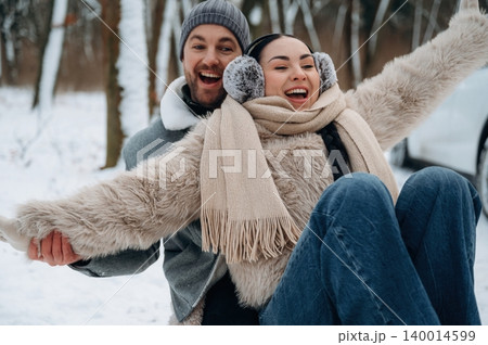 Joyful couple enjoying winter fun, sitting on a sled in snowy landscape, surrounded by trees, capturing the essence of happiness and togetherness in cold weather Joyful couple enjoying winter fun, sitting on a sled in snowy landscape, surrounded by trees, capturing the essence of happiness and togetherness in cold weather 140014599