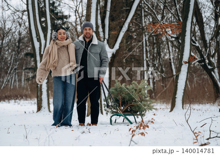 Couple enjoying winter day in snowy forest, pulling sled with evergreen tree, dressed in warm clothing, creating a cozy holiday atmosphere Couple enjoying winter day in snowy forest, pulling sled with evergreen tree, dressed in warm clothing, creating a cozy holiday atmosphere 140014781