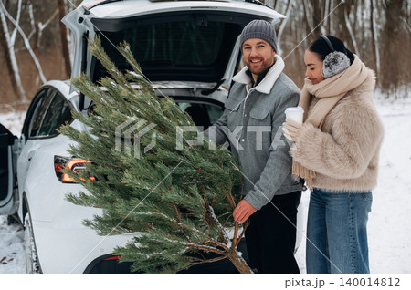 Couple loading a freshly cut Christmas tree into the trunk of a car, surrounded by a snowy landscape, celebrating the holiday spirit and winter joy Couple loading a freshly cut Christmas tree into the trunk of a car, surrounded by a snowy landscape, celebrating the holiday spirit and winter joy 140014812