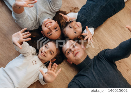 Family enjoying quality time together, lying on wooden floor, smiling and waving hands, capturing joyful moments of togetherness and love Family enjoying quality time together, lying on wooden floor, smiling and waving hands, capturing joyful moments of togetherness and love 140015001