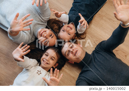 Family enjoying quality time together on the floor, smiling and waving hands, creating a joyful atmosphere of togetherness and connection Family enjoying quality time together on the floor, smiling and waving hands, creating a joyful atmosphere of togetherness and connection 140015002