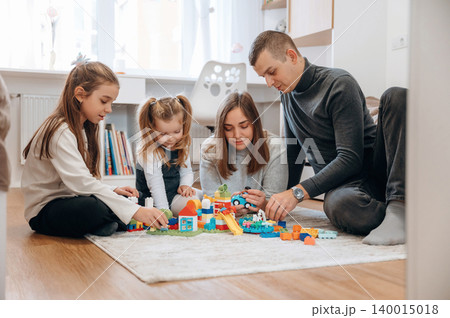 Family engaged in creative playtime with colorful building blocks on a soft rug in a cozy living room, fostering imagination and bonding moments 140015018