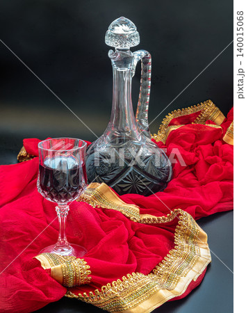 a crystal-cut decanter. Standing at the center, its intricate geometric patterns catch the light while holding a deep, mysterious liquor. Nearby, a matching crystal wine glass rests gracefully, filled a crystal-cut decanter. Standing at the center, its intricate geometric patterns catch the light while holding a deep, mysterious liquor. Nearby, a matching crystal wine glass rests gracefully, filled 140015068