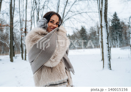 Smiling woman with dark hair wrapped in a cozy fur coat and scarf, enjoying a snowy winter day in a serene forest setting, radiating warmth and joy in the cold Smiling woman with dark hair wrapped in a cozy fur coat and scarf, enjoying a snowy winter day in a serene forest setting, radiating warmth and joy in the cold 140015156
