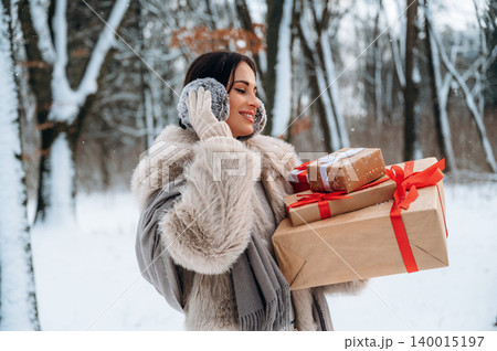 Woman in winter attire, smiling while holding wrapped gifts in a snowy forest, showcasing holiday spirit and joy in a festive outdoor setting Woman in winter attire, smiling while holding wrapped gifts in a snowy forest, showcasing holiday spirit and joy in a festive outdoor setting 140015197