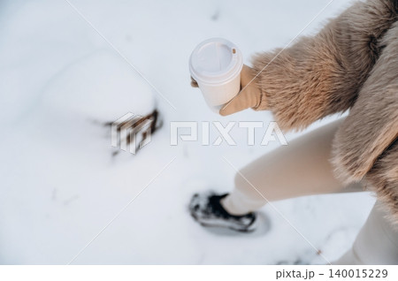 Woman in stylish fur coat holding coffee cup while walking through snowy landscape, showcasing winter fashion and cozy outdoor lifestyle in a serene environment Woman in stylish fur coat holding coffee cup while walking through snowy landscape, showcasing winter fashion and cozy outdoor lifestyle in a serene environment 140015229