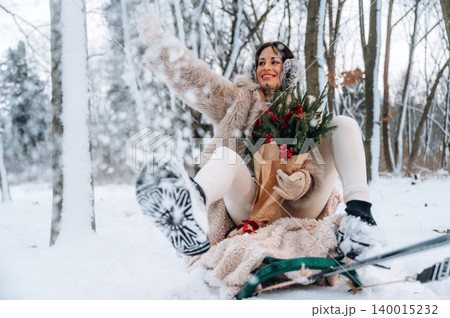 Woman in winter attire, sitting in snow, holding festive greenery with red berries, smiling joyfully, surrounded by snowy trees, capturing the essence of holiday cheer and winter fun Woman in winter attire, sitting in snow, holding festive greenery with red berries, smiling joyfully, surrounded by snowy trees, capturing the essence of holiday cheer and winter fun 140015232