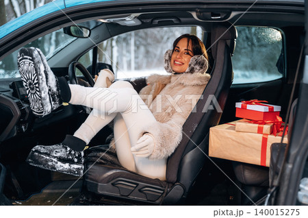 Woman in winter attire, sitting in a car with snowy surroundings, smiling while surrounded by holiday gifts, showcasing festive spirit and cozy atmosphere Woman in winter attire, sitting in a car with snowy surroundings, smiling while surrounded by holiday gifts, showcasing festive spirit and cozy atmosphere 140015275