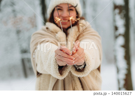 Young woman with brown hair, wearing cozy winter attire, joyfully holding sparklers in a snowy forest, celebrating the festive season with warmth and cheer Young woman with brown hair, wearing cozy winter attire, joyfully holding sparklers in a snowy forest, celebrating the festive season with warmth and cheer 140015627