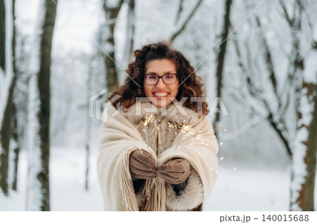 Woman with curly hair, wearing a cozy shawl, joyfully holding sparklers in a snowy forest, celebrating winter festivities with a cheerful expression and magical ambiance Woman with curly hair, wearing a cozy shawl, joyfully holding sparklers in a snowy forest, celebrating winter festivities with a cheerful expression and magical ambiance 140015688