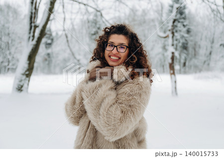 Smiling woman with curly hair wearing a cozy fur coat and gloves, standing in a snowy landscape, showcasing winter fashion and joyful ambiance in a serene environment Smiling woman with curly hair wearing a cozy fur coat and gloves, standing in a snowy landscape, showcasing winter fashion and joyful ambiance in a serene environment 140015733