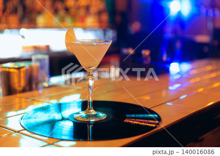 Orange coupe cocktail on vinyl record with bright blue neon bar background. 140016086