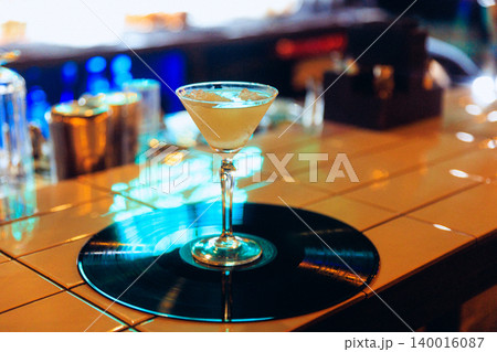 Coupe cocktail on vinyl record at neon bar counter with nightlife reflections 140016087