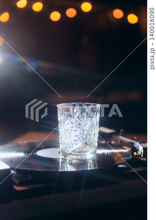 Empty crystal whiskey glass on vinyl record with dramatic nightclub bokeh lights. Empty crystal whiskey glass on vinyl record with dramatic nightclub bokeh lights. 140016090
