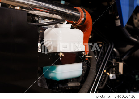 Close Up of White Plastic Fluid Reservoir and Orange Hose in Heavy Duty Industrial Engine Compartment 140016416