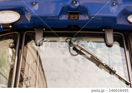 Close up of blue tractor windshield with wiper and modern camera sensor for agricultural technology Close up of blue tractor windshield with wiper and modern camera sensor for agricultural technology 140016495