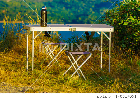 Outdoor table and chairs set up next to a river during daylight in a green landscape Outdoor table and chairs set up next to a river during daylight in a green landscape 140017051
