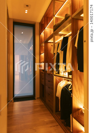 Modern illuminated walk in closet interior with shelves and warm lighting 140017174