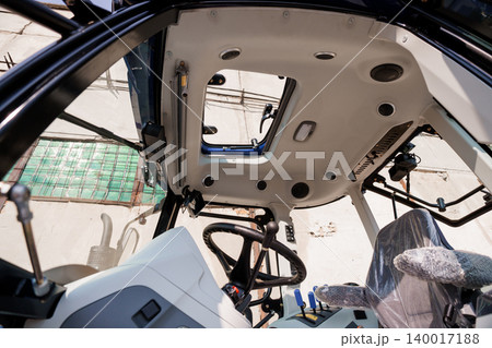Interior View of Modern Agricultural Tractor Cabin with Steering Wheel and Control Panel in Daylight 140017188