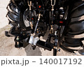 Close Up of Black Tractor Rear Hitch Mechanism and Large Rubber Tires on Dirt Ground 140017192