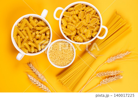 Assorted dry pasta types with wheat ears on yellow background 140017225