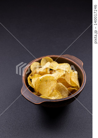 Crinkle cut potato chips filling rustic bowl on dark background Crinkle cut potato chips filling rustic bowl on dark background 140017246