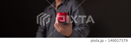 Man hand holding red heart shape on dark background. Concept of love, healthcare, medical insurance and charity donation. Valentine's day symbol for romantic relationship and kindness support. Man hand holding red heart shape on dark background. Concept of love, healthcare, medical insurance and charity donation. Valentine's day symbol for romantic relationship and kindness support. 140017379