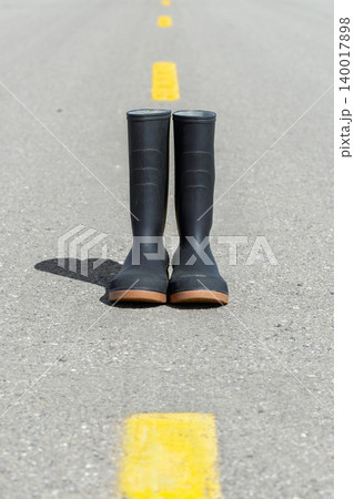 Tall rubber boots on the asphalt highway with yellow line. Tall rubber boots on the asphalt highway with yellow line. 140017898