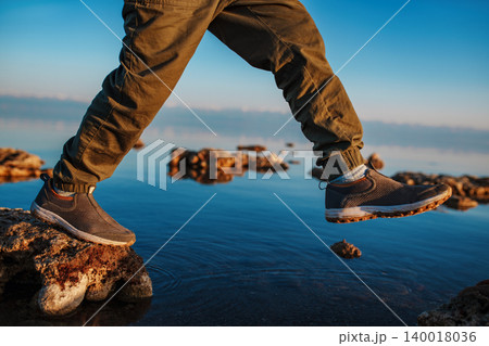 Boy walking on stones in the lake, close-up focus on boots Boy walking on stones in the lake, close-up focus on boots 140018036