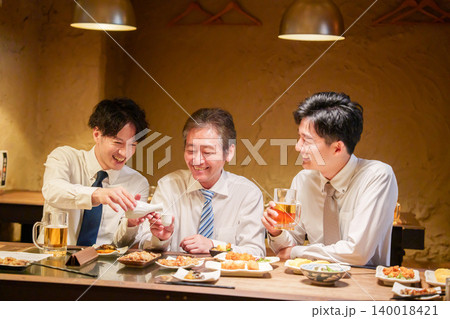 居酒屋で先輩にお酌をする若手社員 居酒屋で先輩にお酌をする若手社員 140018421