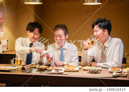 居酒屋で先輩にお酌をする若手社員 居酒屋で先輩にお酌をする若手社員 140018425