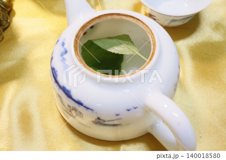 Teapot with Leaf in Water on Yellow Fabric Teapot with Leaf in Water on Yellow Fabric 140018580
