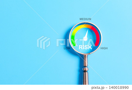 Business Risk Assessment and Management Concept. A magnifying glass highlighting a risk level gauge on a blue background, indicating low, medium, and high risk for business assessment purposes. 140018990