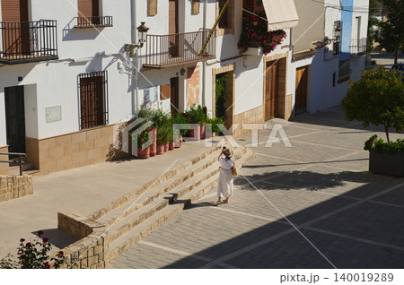 Woman traveling in a small Spanish village with whitewashed houses, stone steps and sunlit street Woman traveling in a small Spanish village with whitewashed houses, stone steps and sunlit street 140019289