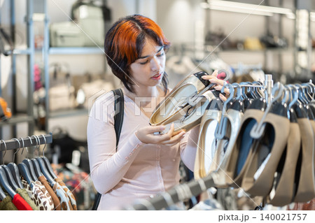 Attentive young girl choosing shoes in clothing store Attentive young girl choosing shoes in clothing store 140021757